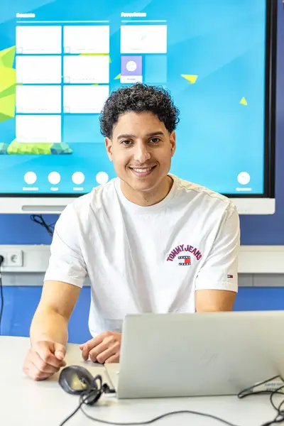 Student achter laptop in leslokaal met scherm met agenda op de achtergrond