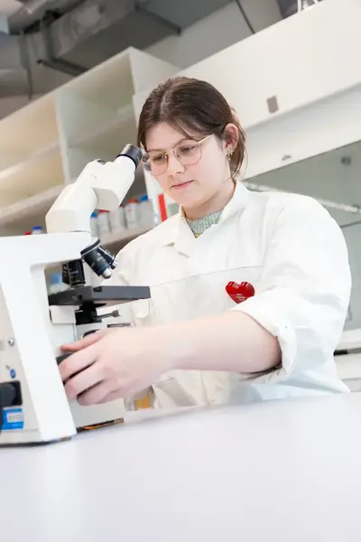 Studente in laboratoriumjas achter microscoop