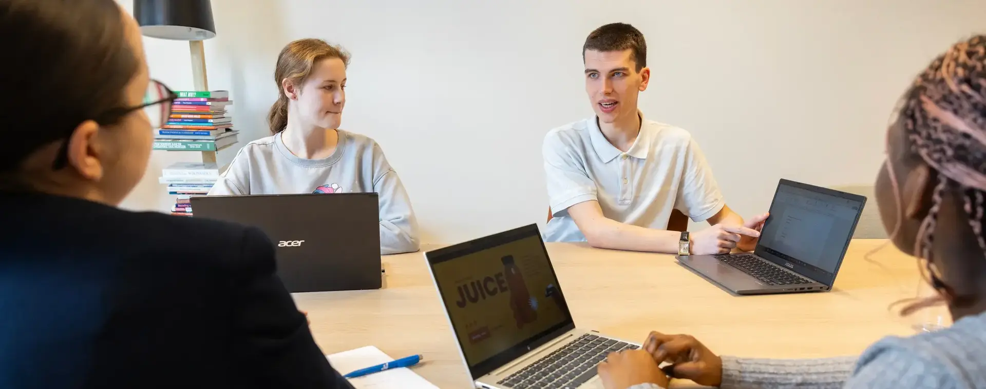 Meerdere studenten zitten aan tafel met hun laptops