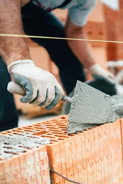 Man is met cement en stenen een muur aan het mestelen