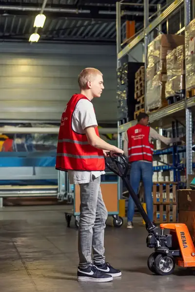 Jongeman in magazijn houdt een mini vorklift met goederen vast.
