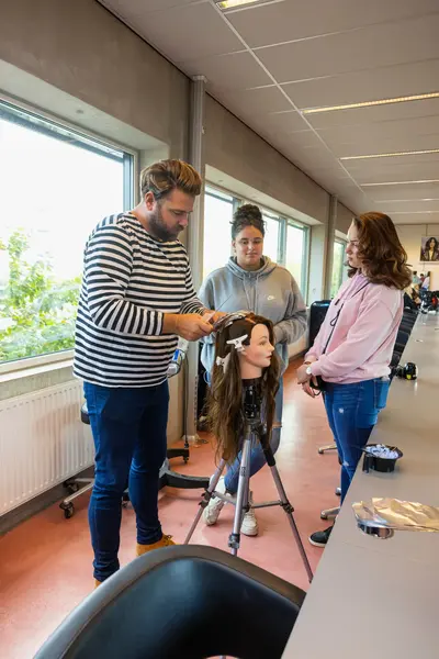 Docent geeft les aan kappersstudenten met behulp van een dummy.
