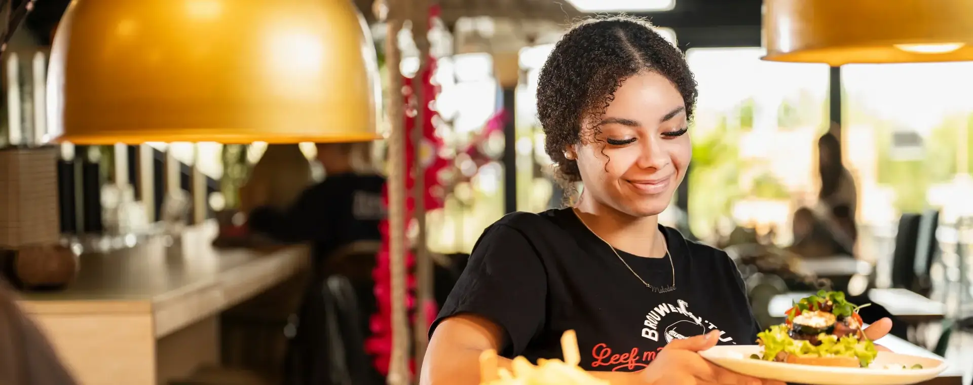 Student in de horeca serveert met een glimlach een gerecht aan tafel in een restaurant