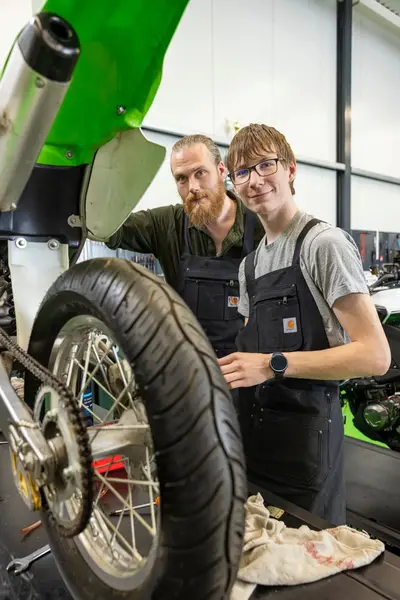 Docent en student poseren naast motorfiets in garage
