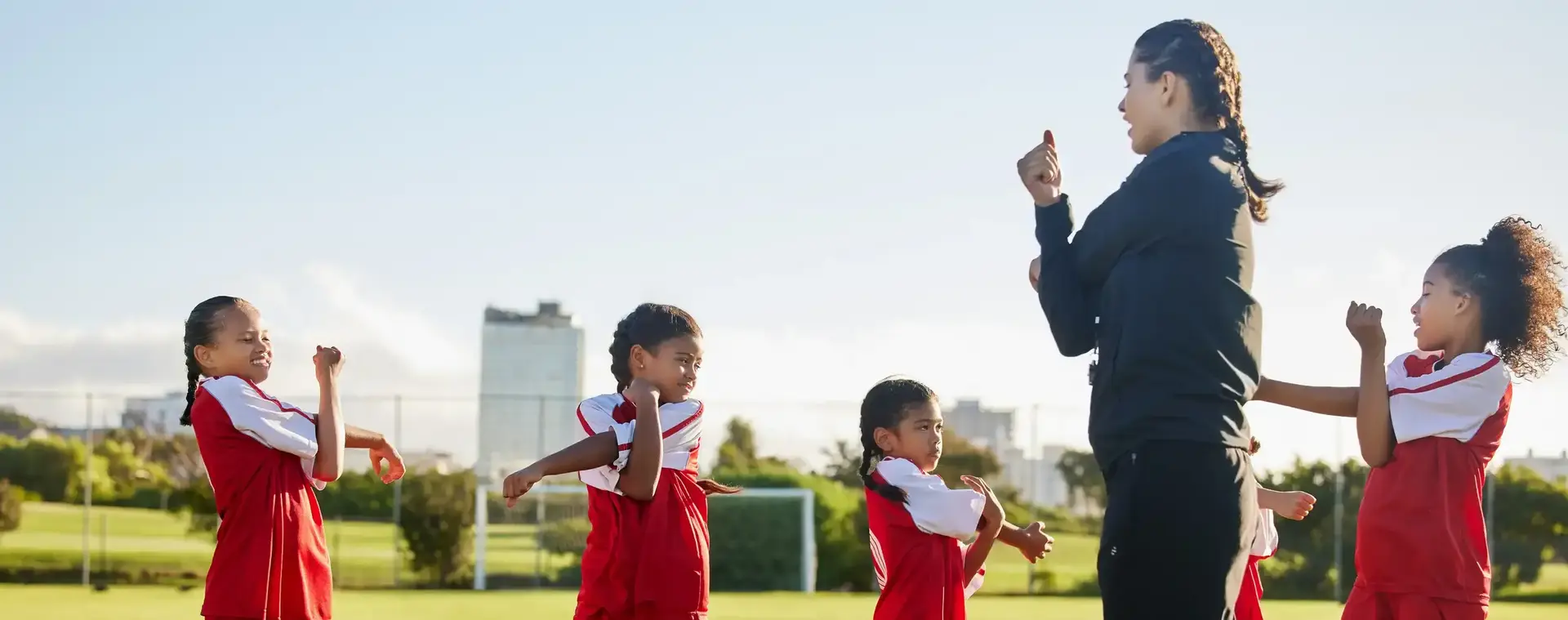 Vrouwelijke voetbaltrainer doet met vier kinderen in voetbaltenues stretch oefeningen op het voetbalveld om op te warmen.