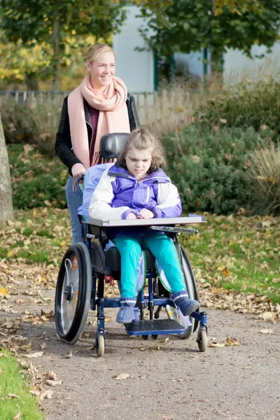 Student duwt meisje in rolstoel door park