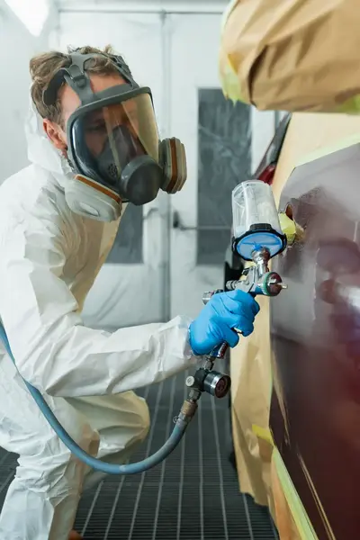 Student in wit beschermingspak en gezichtsmasker spuit verf op auto