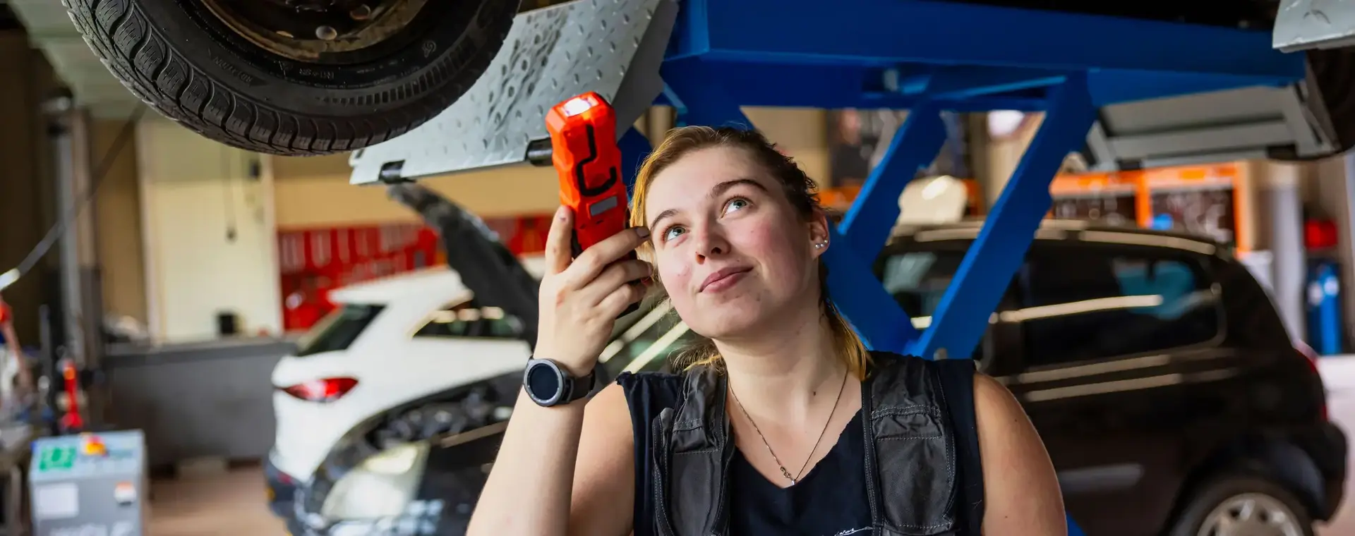 Studente autoschadehersteller kijkt onder auto die op reparatiebrug staat