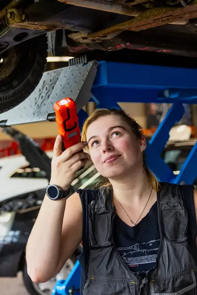 Studente autoschadehersteller kijkt onder auto die op reparatiebrug staat