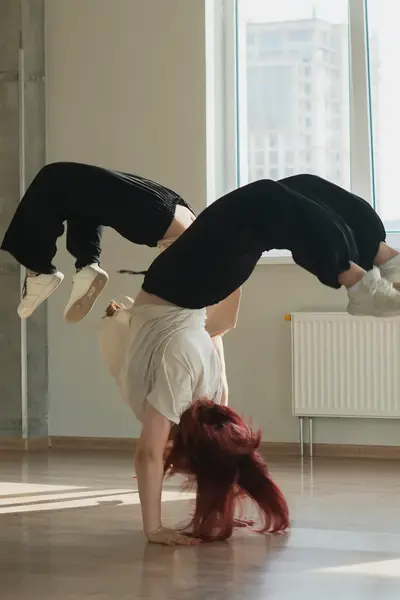 Student voert een indrukwekkende breakdance-move uit op de vloer van een dansstudio, waarbij zij ondersteboven balanceert op haar handen.