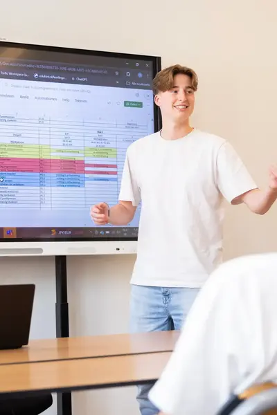 Een student geeft een presentatie aan klasgenoten met een groot scherm waarop een schema te zien is.