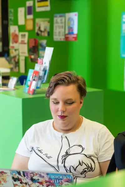 Student met rode lippenstift zit in een groene kamer achter een laptop te werken.
