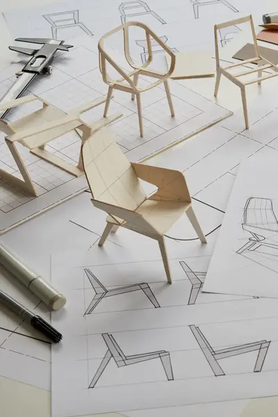 Ontwerpschetsen en maquettes van stoelen liggen op tafel.