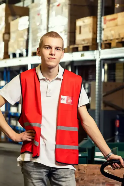 Student met rode veiligheidshesje staat met palletwagen in een magazijn.