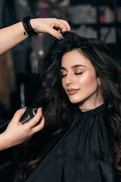 Studente haarstylist spuit haarlak in haar model