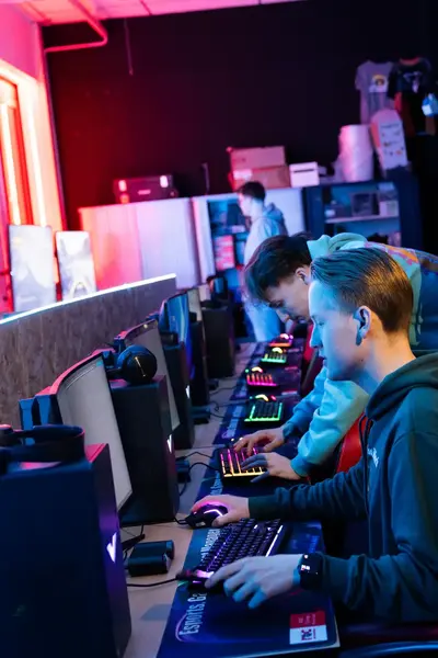 Meerdere studenten achter computers in een game klaslokaal. Docent kijkt toe en geeft aanwijzingen.