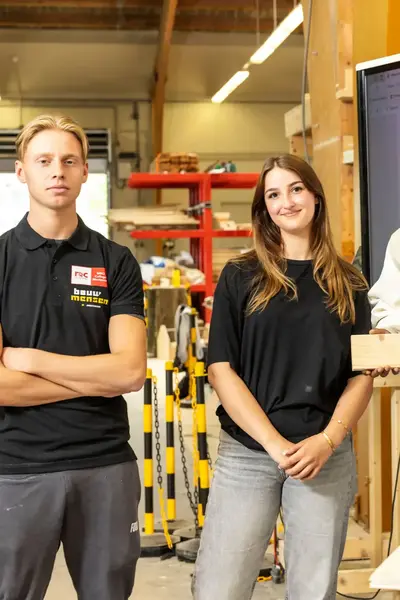 Vier studenten in een bouwlokaal presenteren hun werkstuk met een bouwtekening op het scherm op de achtergrond.