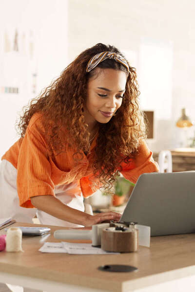 Jonge ondernemer werkt op laptop tussen kleding en dozen.