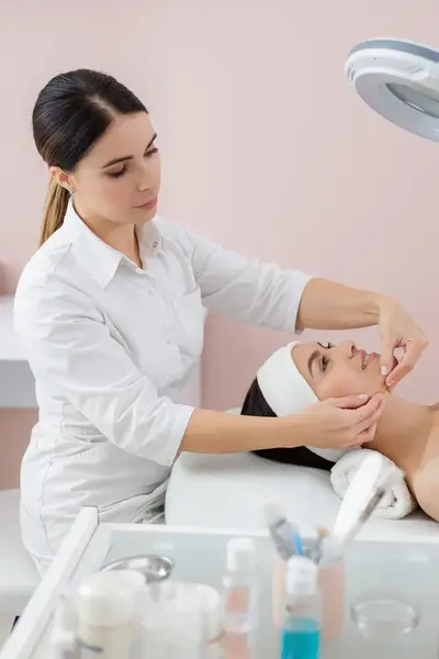 Schoonheidsspecialiste verzorgt gezicht client in kliniek