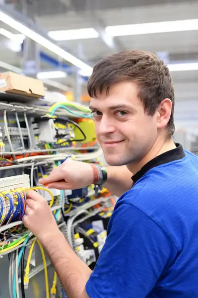 Man sleutelt aan elektrotechnische installatie en lacht in camera