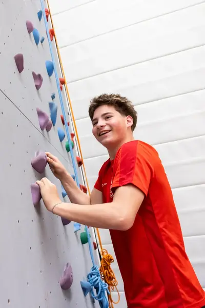 Student in rood shirt op klimmuur