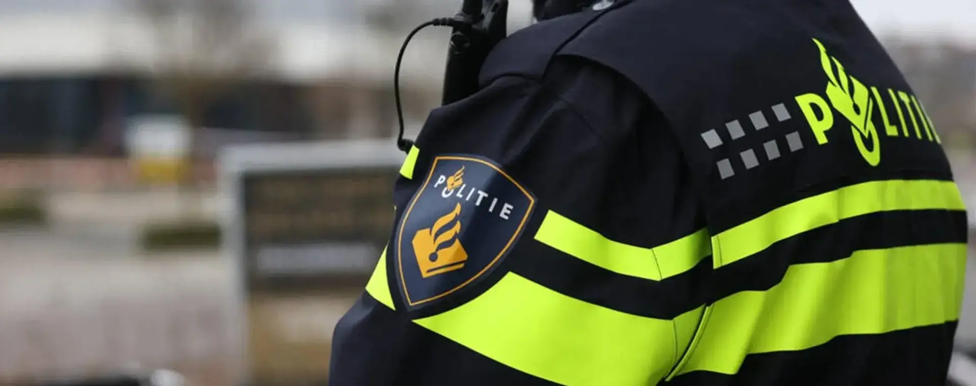 Close-up van de arm van een politieagent in uniform, met het politielogo duidelijk zichtbaar op de mouw. 