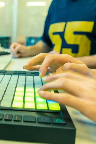 Student werkt met een MIDI-controller in een muziekstudio, terwijl op de achtergrond muzieksoftware op een laptop draait.