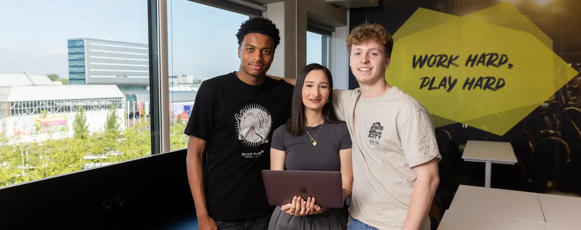 Drie studenten in hoogbouw staan bij een raam 