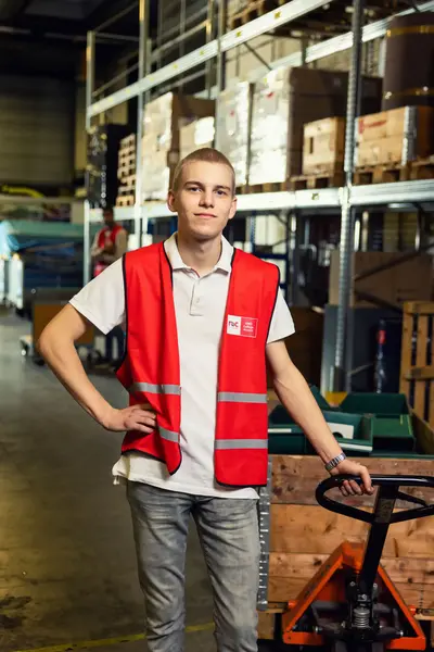 Jongen met zijn hand op zijn zij naast een vorkheftruck in een magazijn.