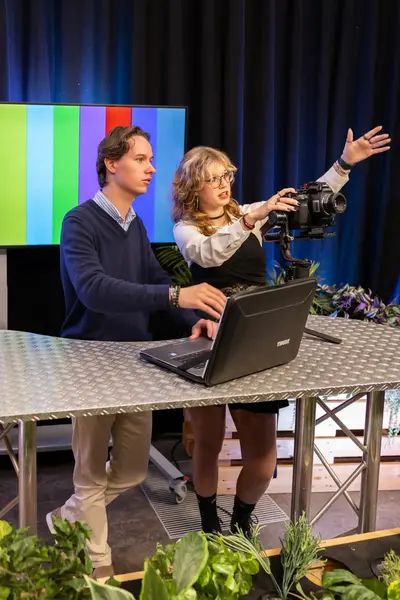 Een docent wijst iets aan terwijl de student achter een laptop zit.
