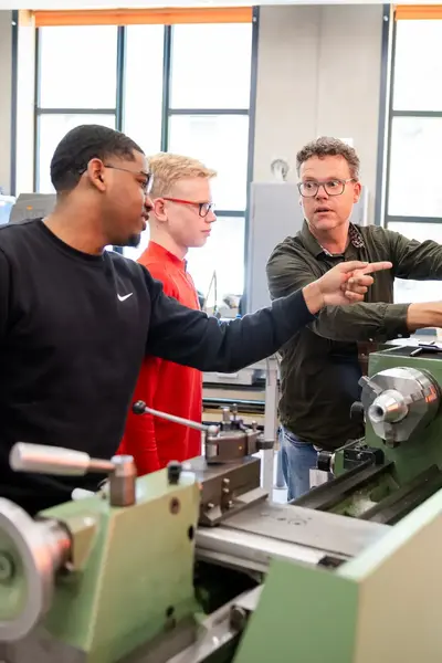 Docent mechatronica geeft les aan twee studenten in praktijkruimte vol machines. 