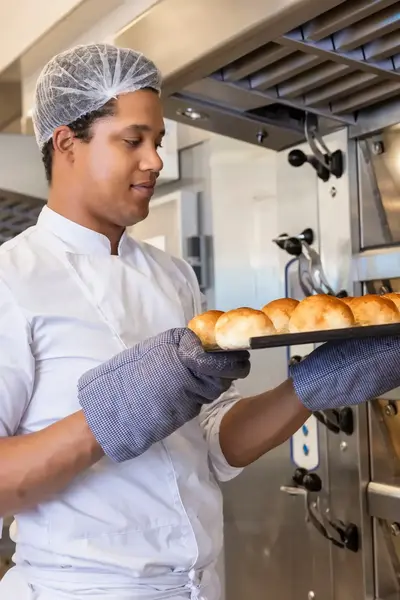 Bakker met ovenhandschoenen plaatst versgebakken broodjes in rek
