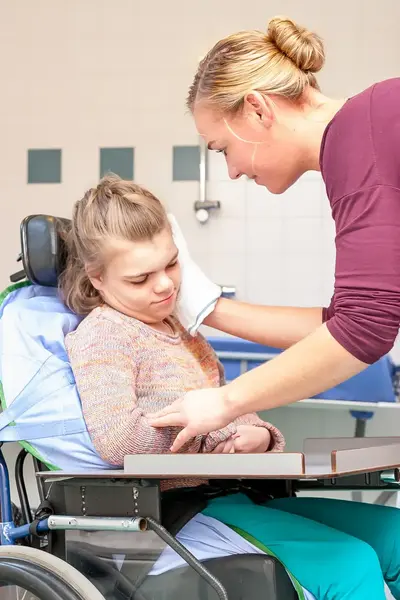 Verzorgster wast gezicht meisje in rolstoel.