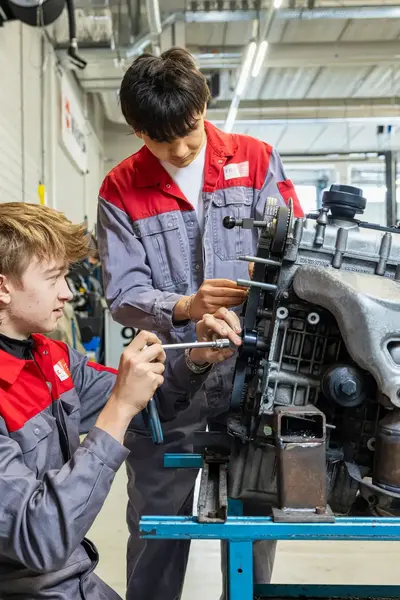 Twee studenten in ROCvA-overall sleutelen aan motorblok in garage
