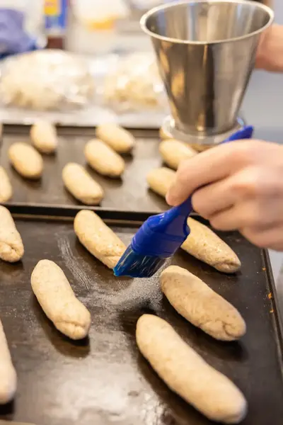 Pistoletjes op bakplaat worden ingesmeerd met eigeel