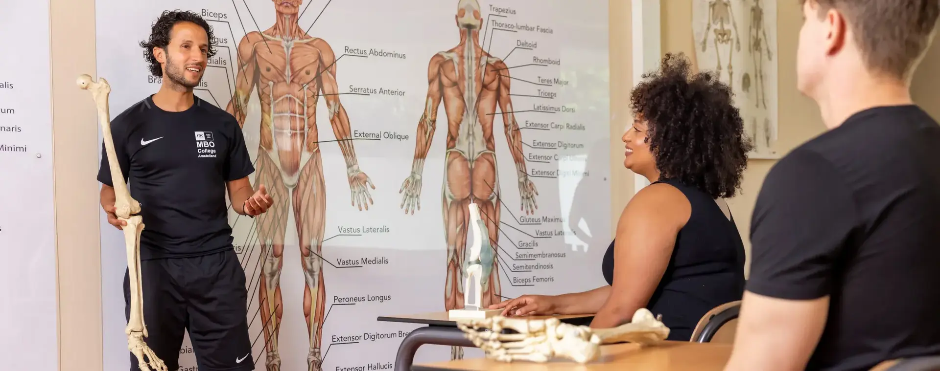Docent voor een klas met poster anatomie menselijk lichaam op achtergrond.