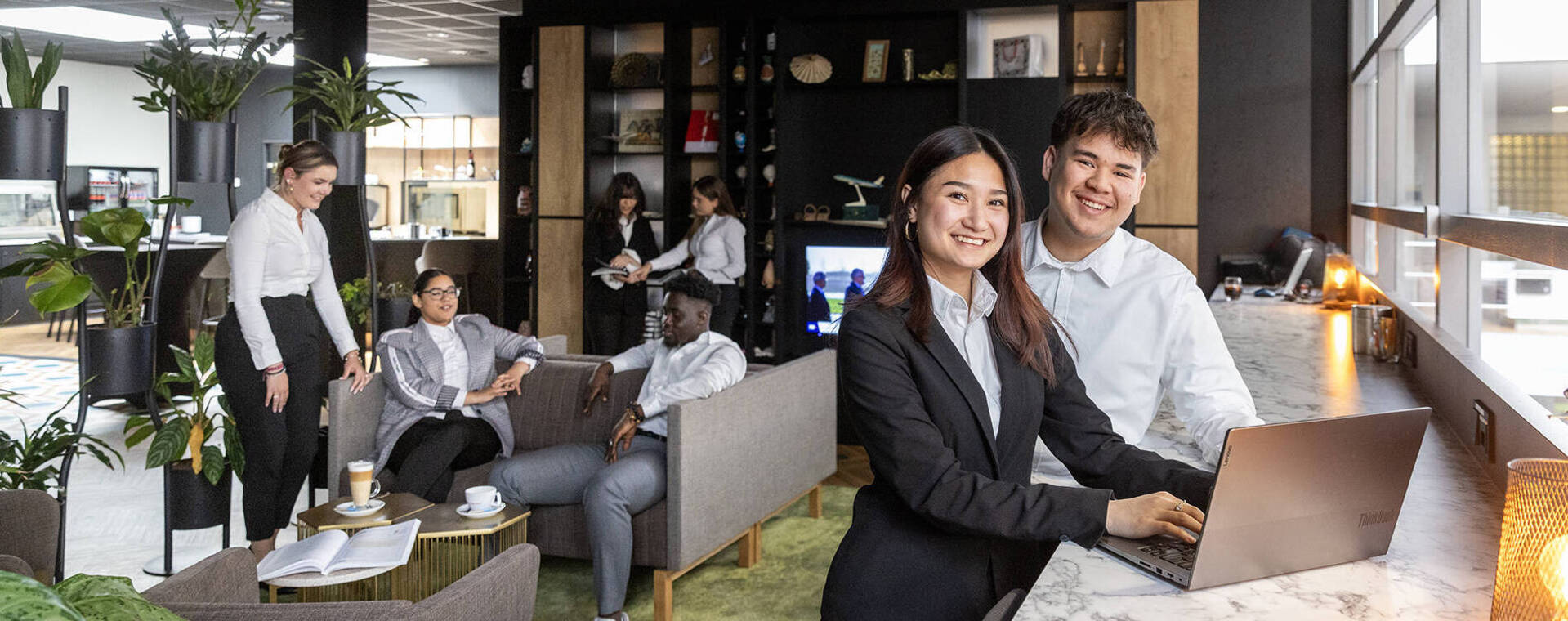Twee studenten achter balie met laptop lounge-achtergrond met gasten