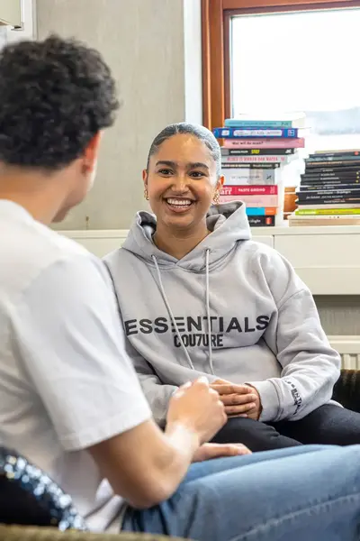 Twee studenten zitten samen op een bank en praten met elkaar.