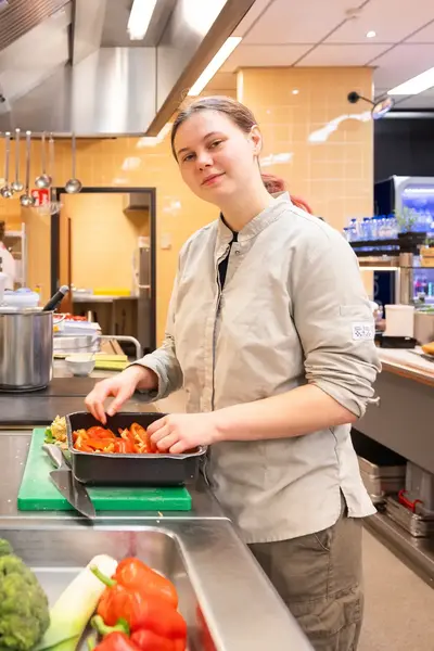 Student in bedrijfskleding snijdt tomaten in een kantine.