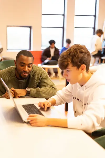 Studenten werken samen met docent op laptops in een klaslokaal.