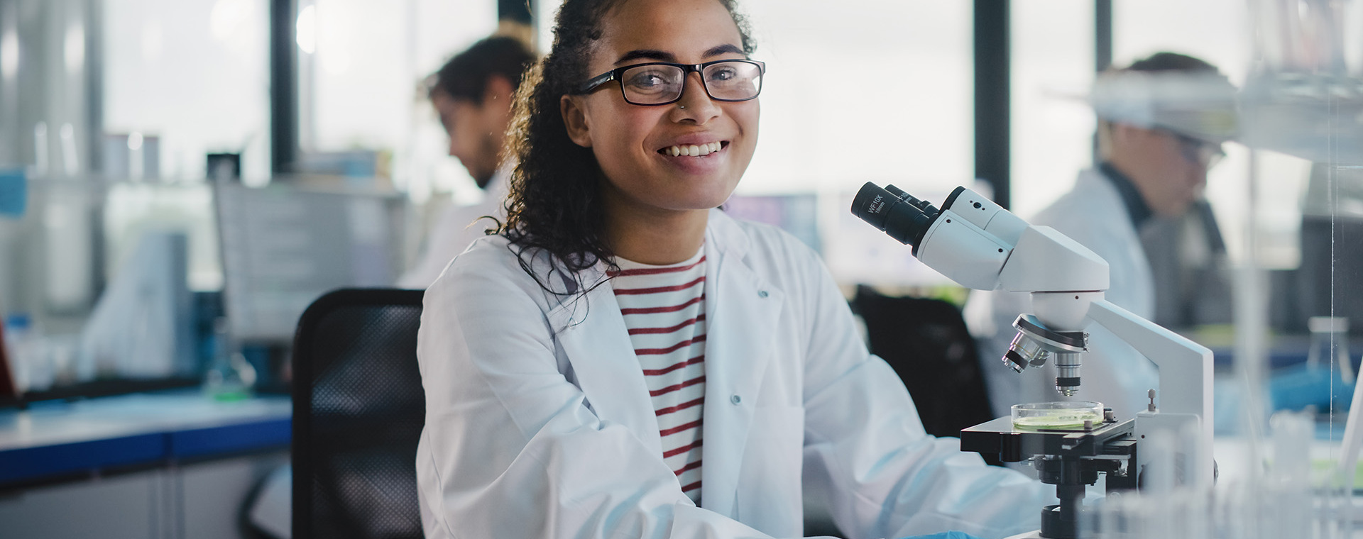 Meisje in witte laboratoriumjas met een microscoop