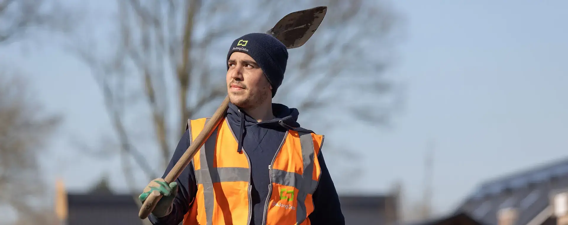Man buiten met oranje hesje en schep