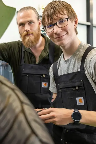Student en begeleider werken samen aan een motorfiets op een werkplaats.