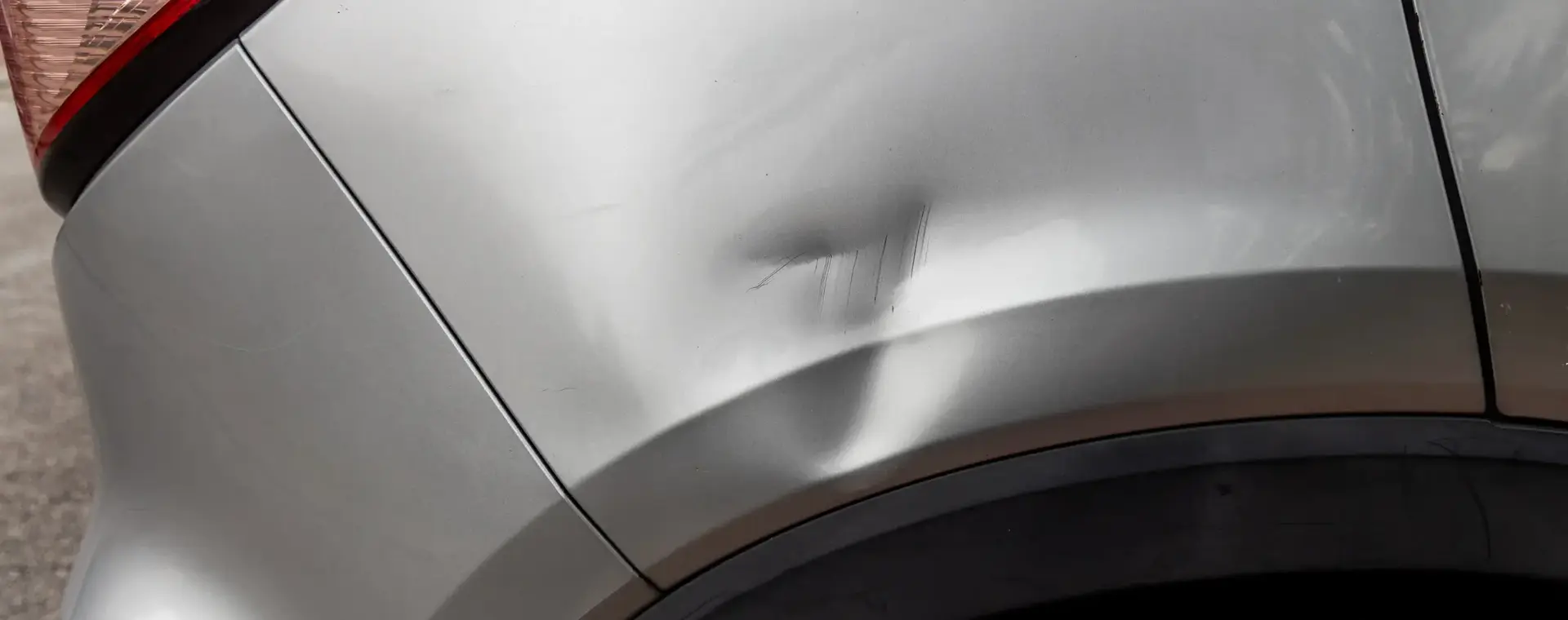 Deuk in carrosserie bij rechterachterband grijze auto