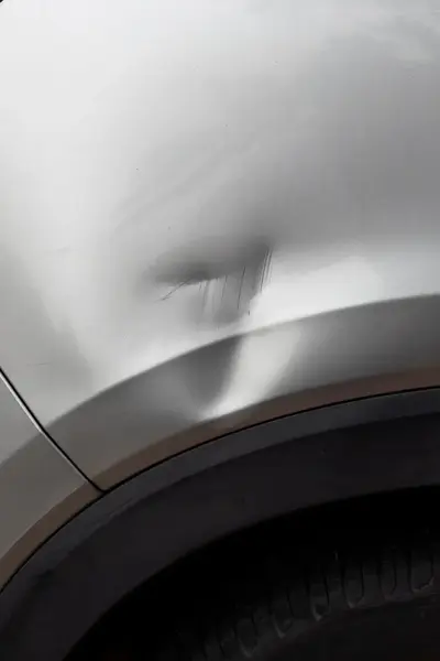 Deuk in carrosserie bij rechterachterband grijze auto