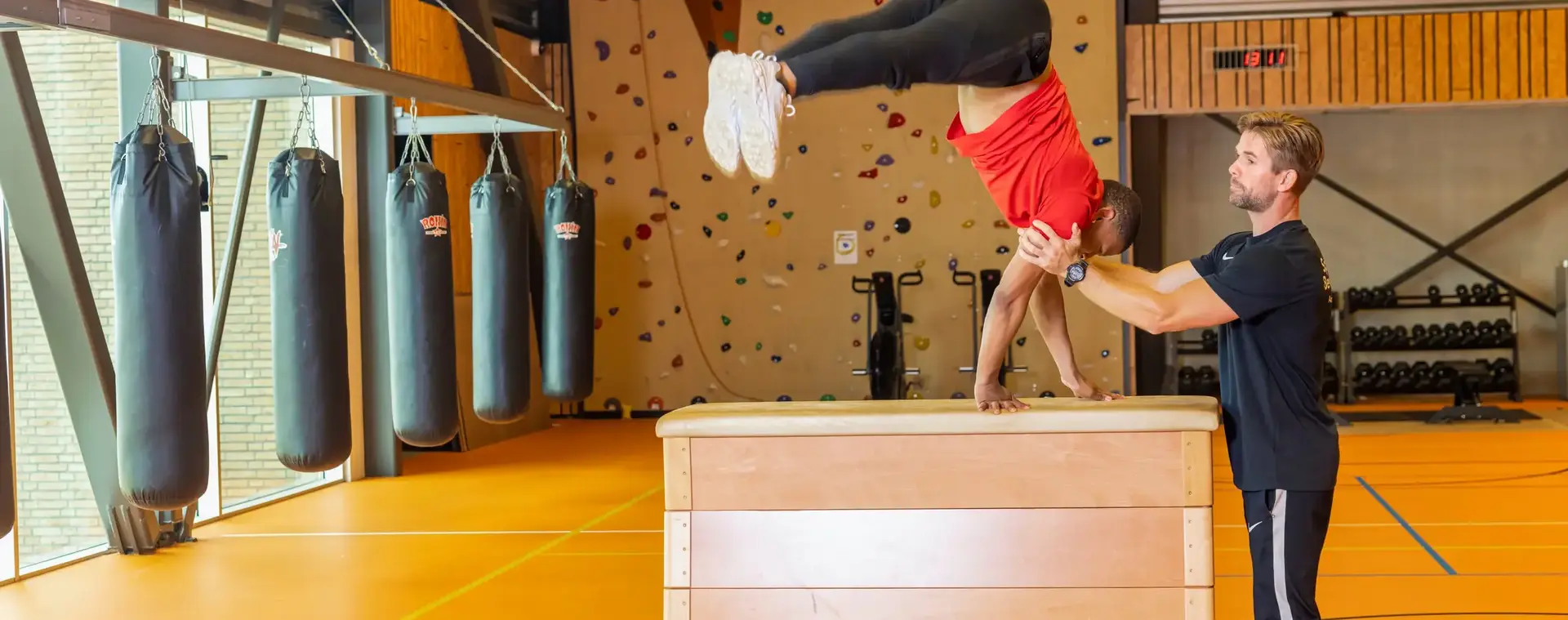Docent met student in gymzaal doen een oefening op de bok.