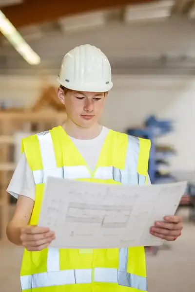 Student in geel hesje inspecteert bouwtekening op bouwplaats