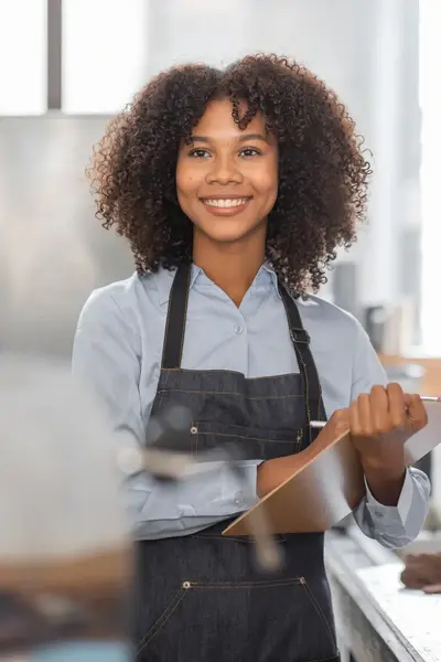 Medewerker in een horecakeuken met schort en notitieblok staat klaar om bestellingen op te nemen.