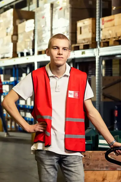 Jongen in oranje hesje met steekwagen in groot magazijn