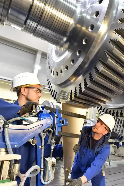 Twee studenten met helmen en veiligheidsbril staan onder levensgrote gasturbine